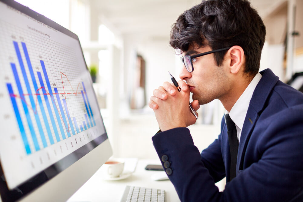 Trader sitting in front of a computer screen displaying a trading chart, thinking about how to earn 5000 per day from the stock market.