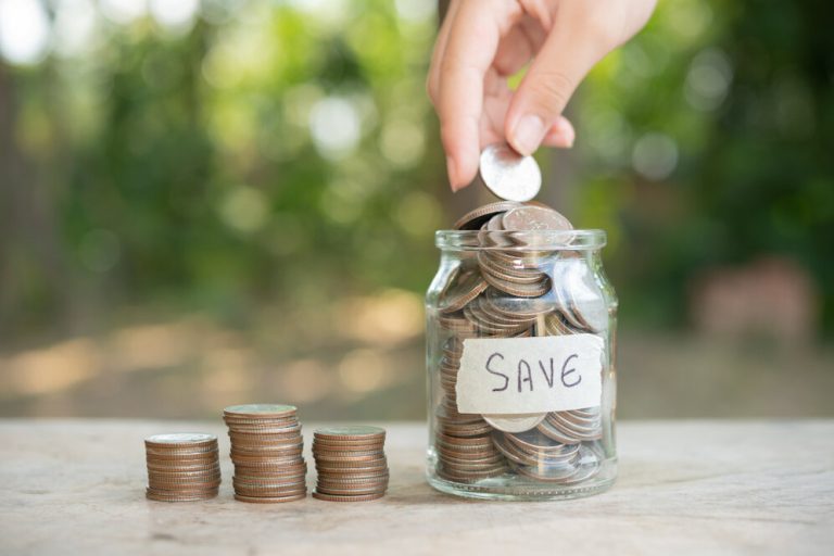 A person putting coins into a glass jar labeled ‘Save’, symbolizing financial growth and the benefits of saving money early for future security.